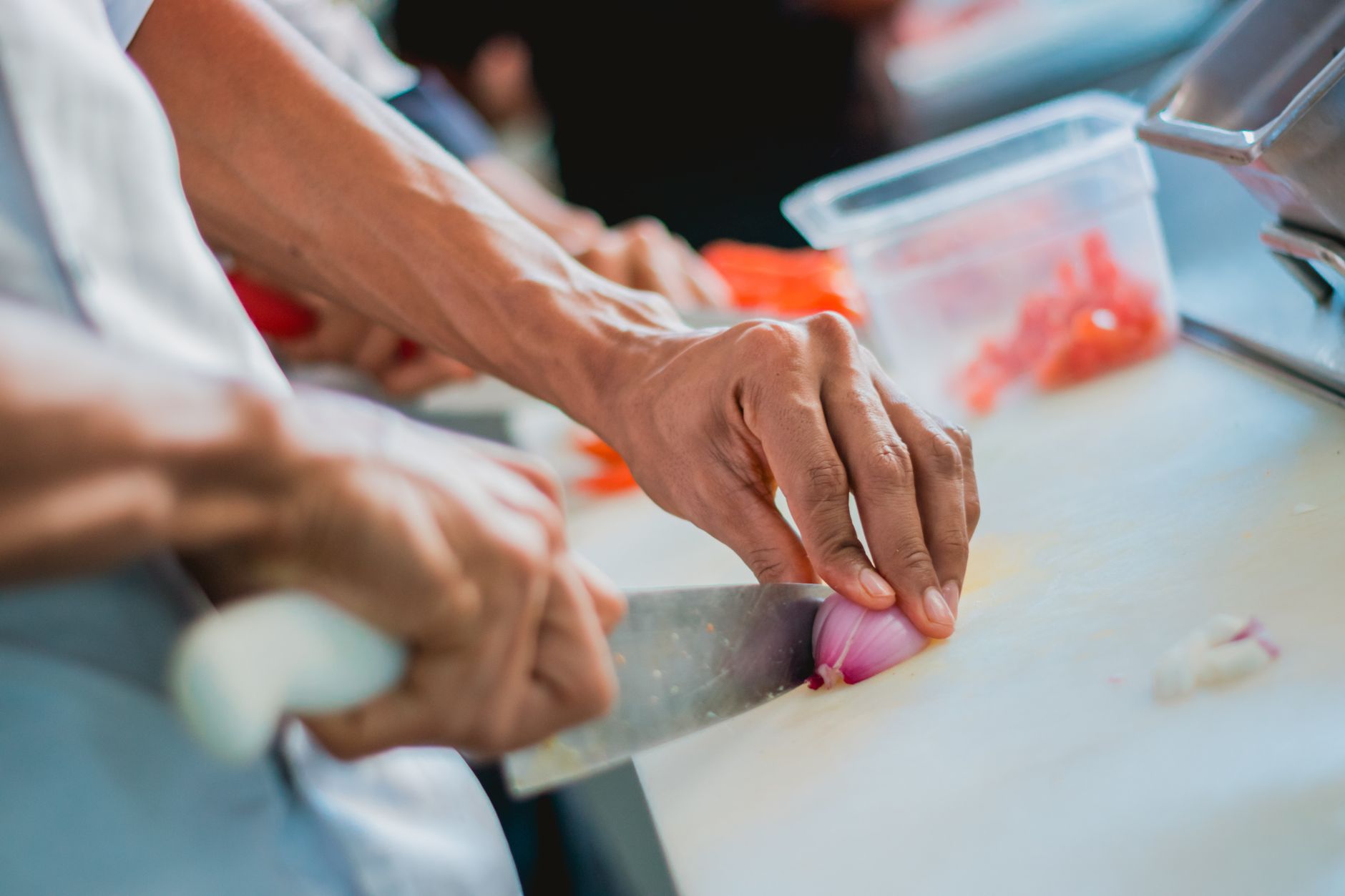 Close-up of a chef slicing onion in a kitchen setting, emphasizing food preparation.