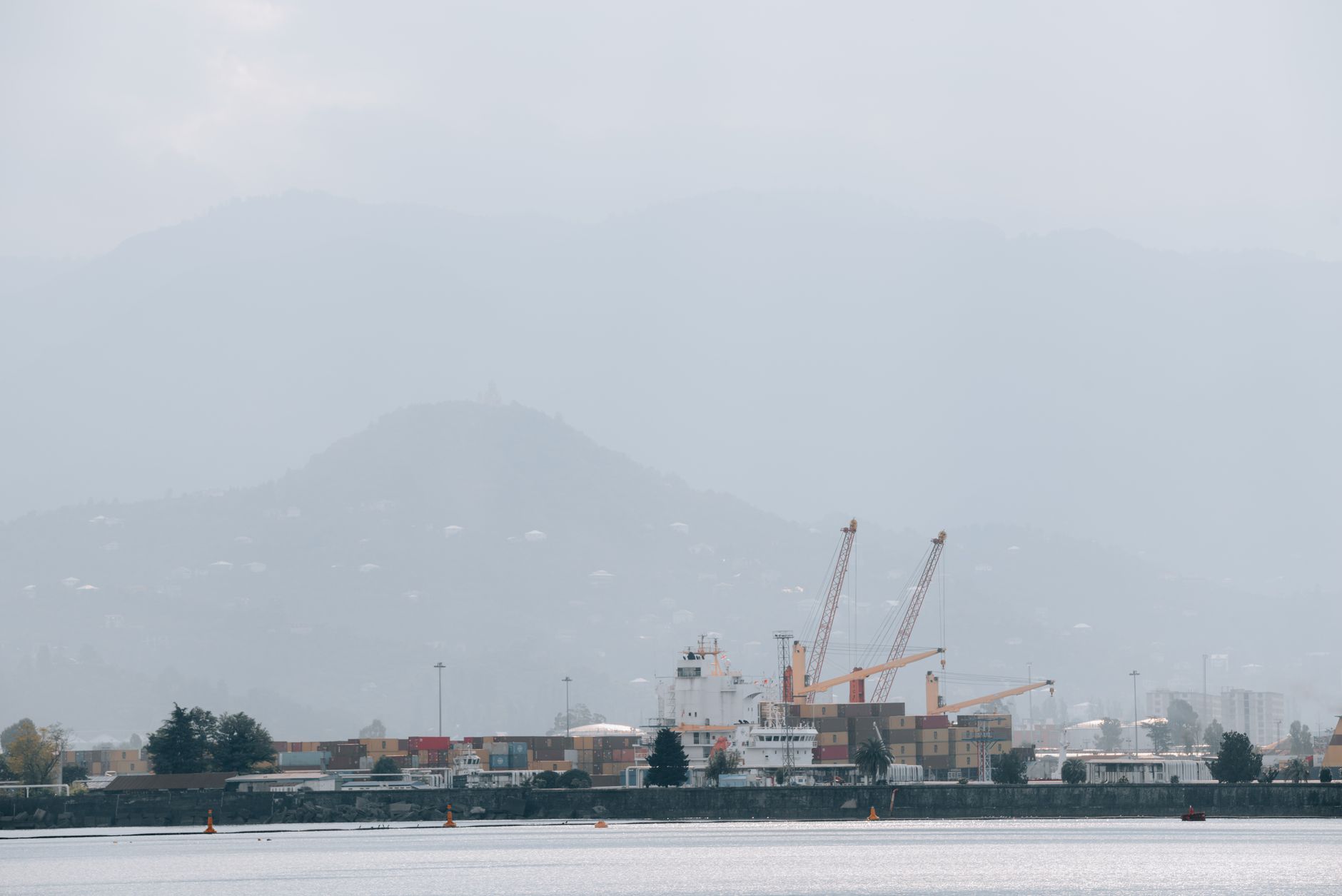 A foggy port scene with cranes, shipping containers, and mountains in the background.