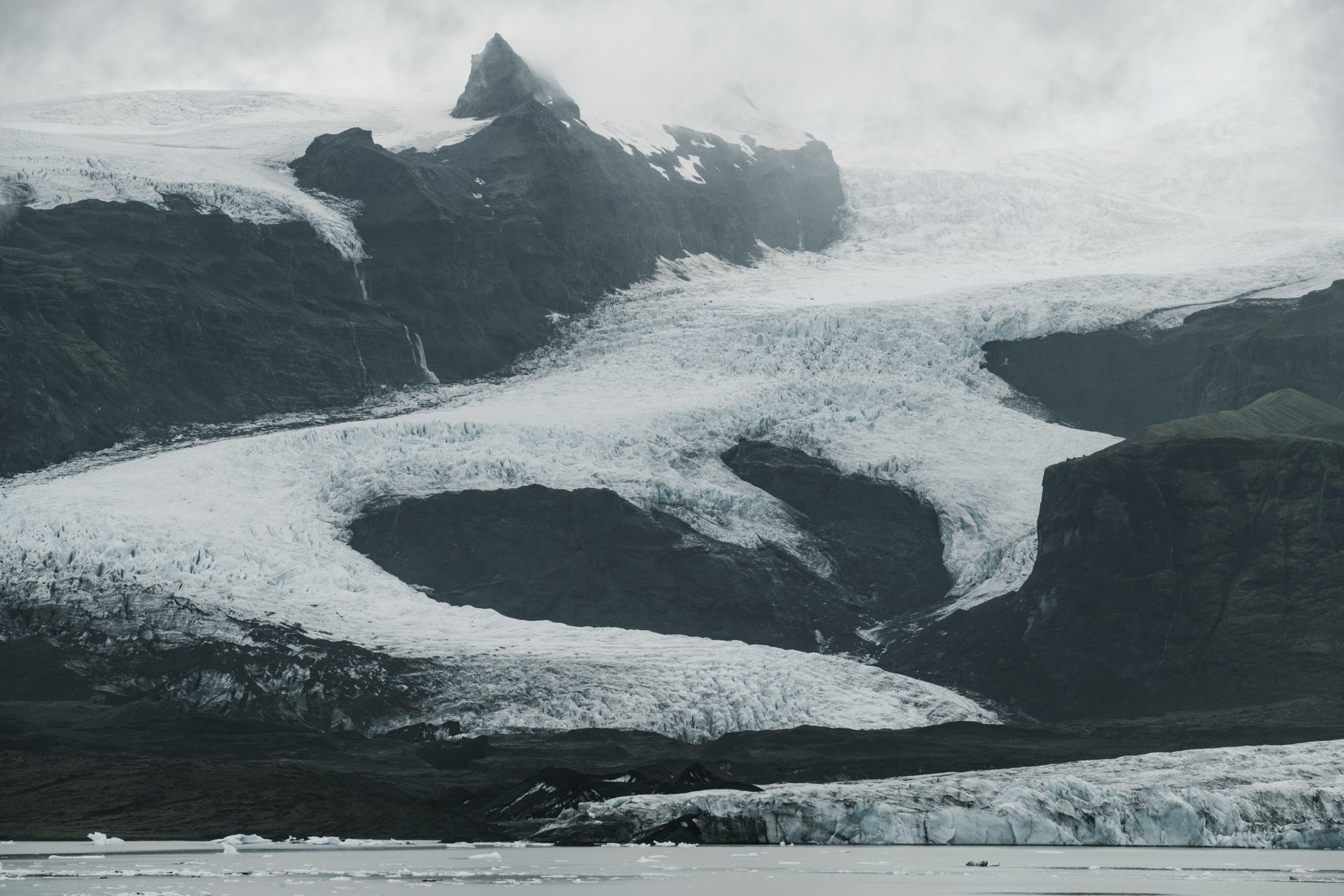 Severe Nordic landscape of snowy mountain slopes covered with ice located near cold sea with black and white effect