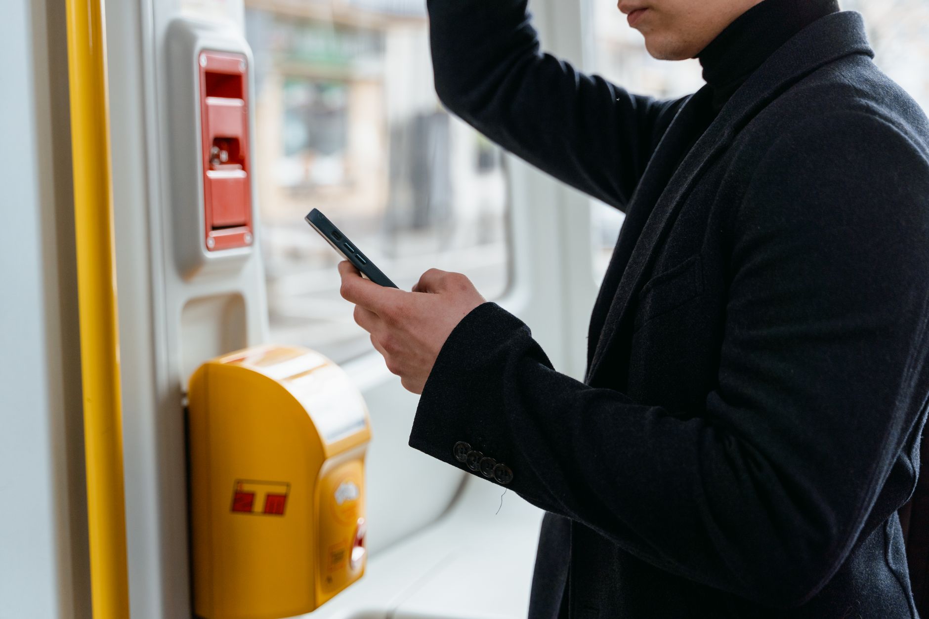 Adult in a black coat checking smartphone while commuting on public transport.