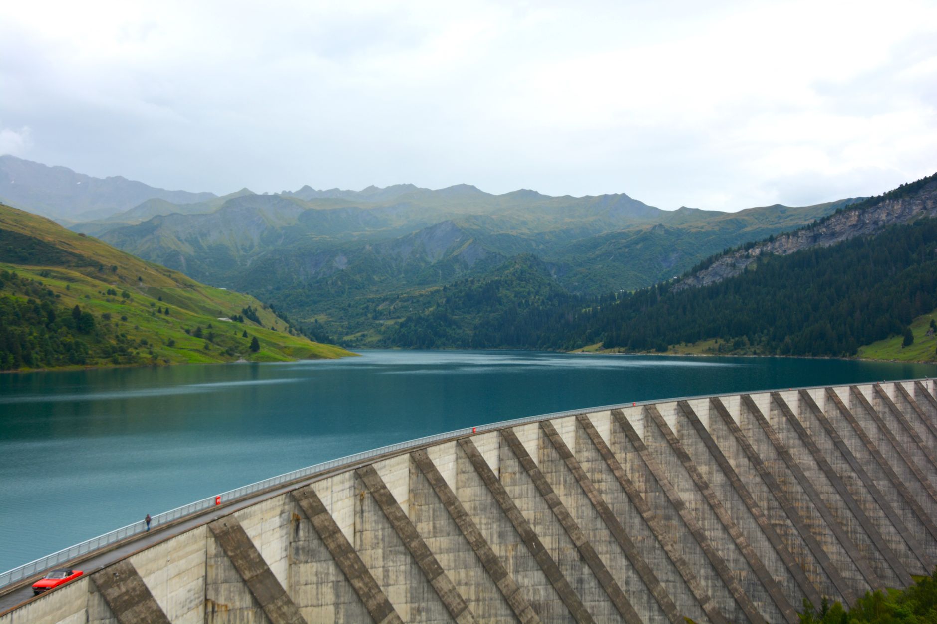 A scenic mountain landscape featuring a large dam and serene lake reflection.