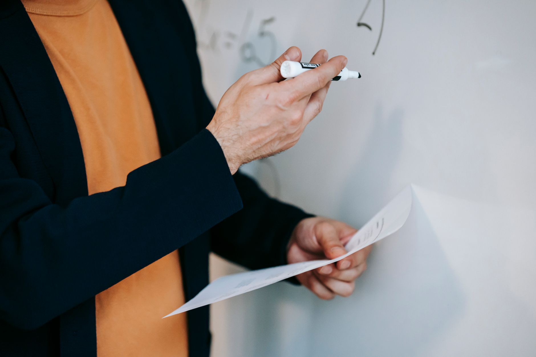 Close-up of a teacher explaining math concepts on a whiteboard while holding notes.