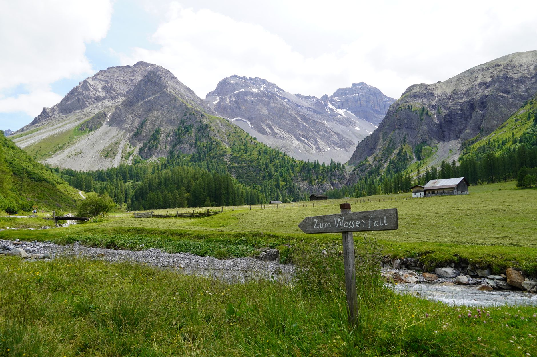 Signpost guiding path through lush Swiss alpine landscape with majestic mountains.