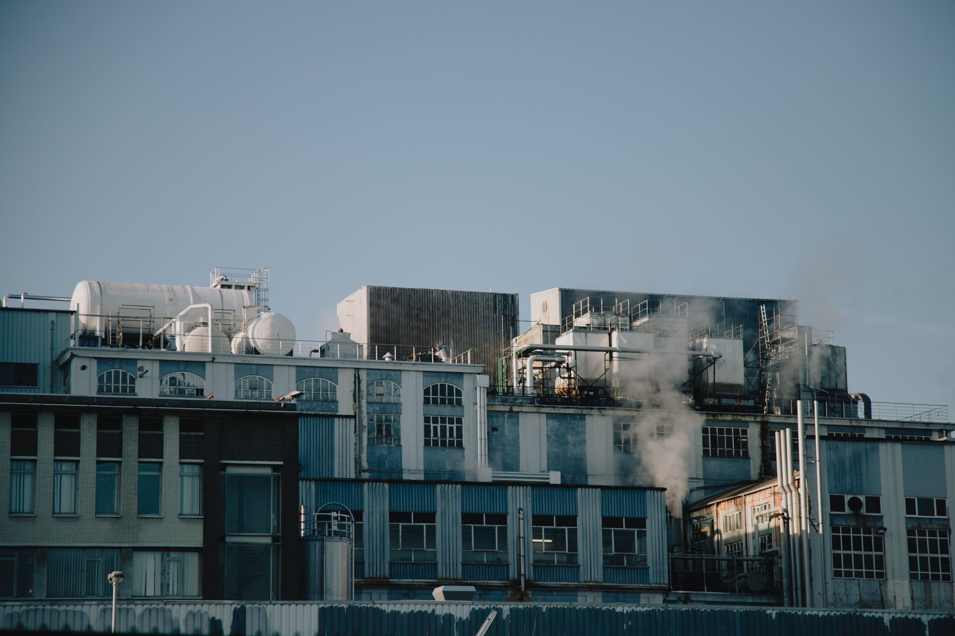 Exterior of aged industrial building with metal pipes and barrels against cloudless blue sky