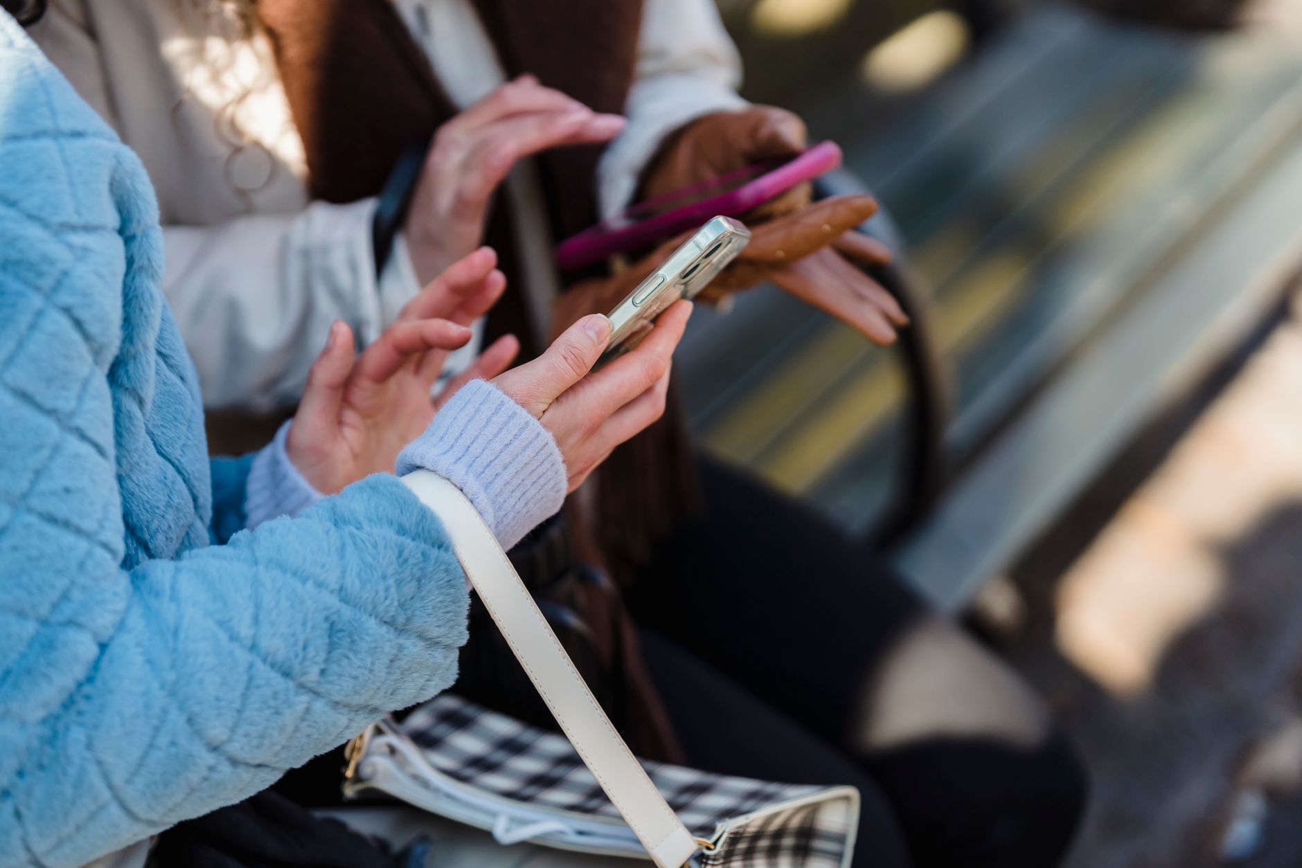 From above of crop anonymous friends sharing information on mobile phones in park in daytime on blurred background
