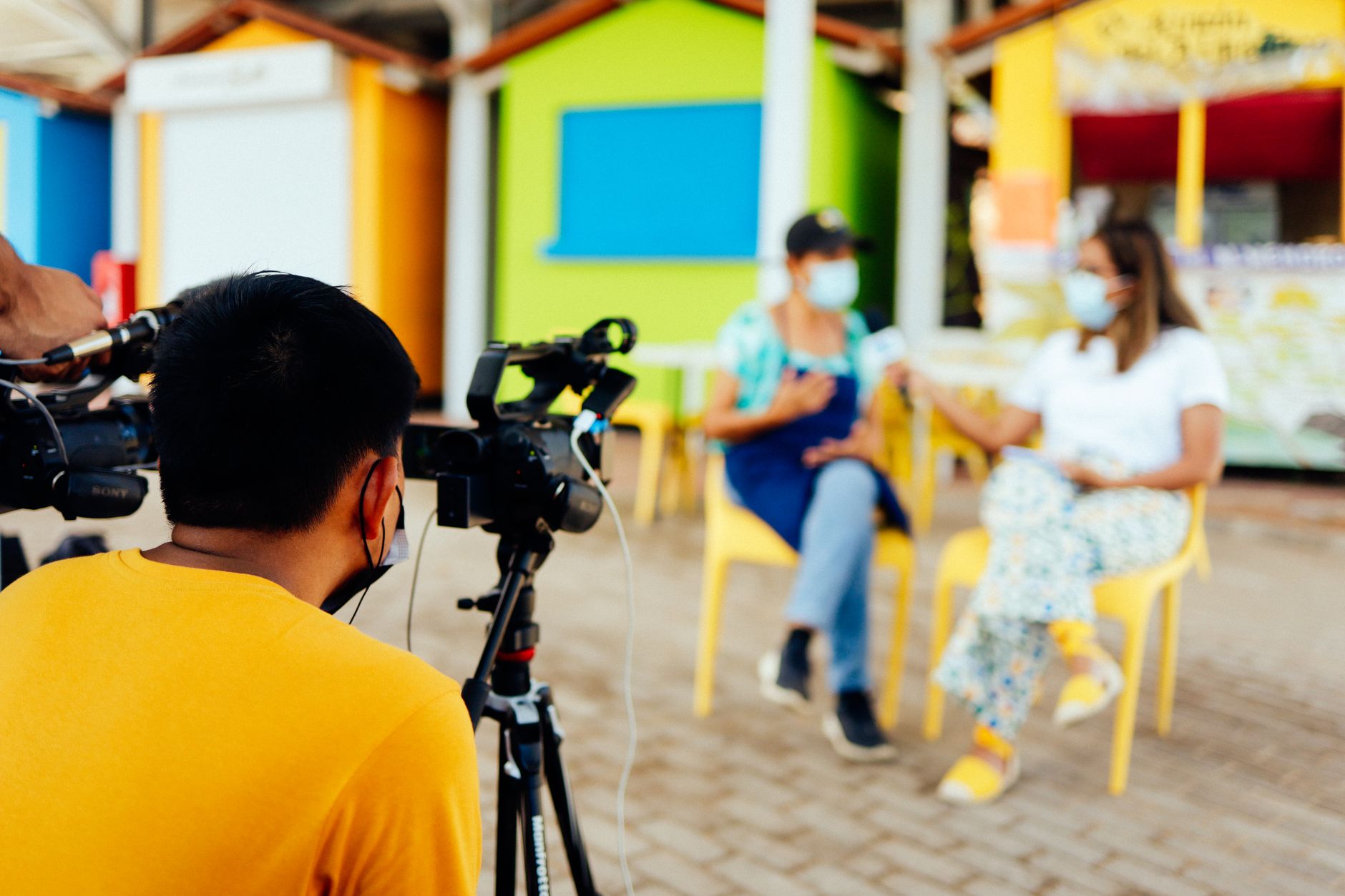 Camera crew filming an outdoor interview with masked participants for a documentary.