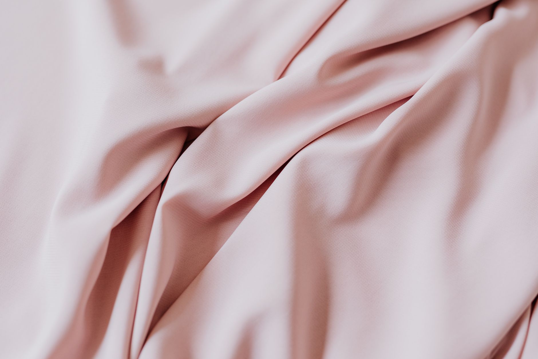 Close-up view of a soft pink fabric with smooth, elegant draping and folds, perfect for textile design.