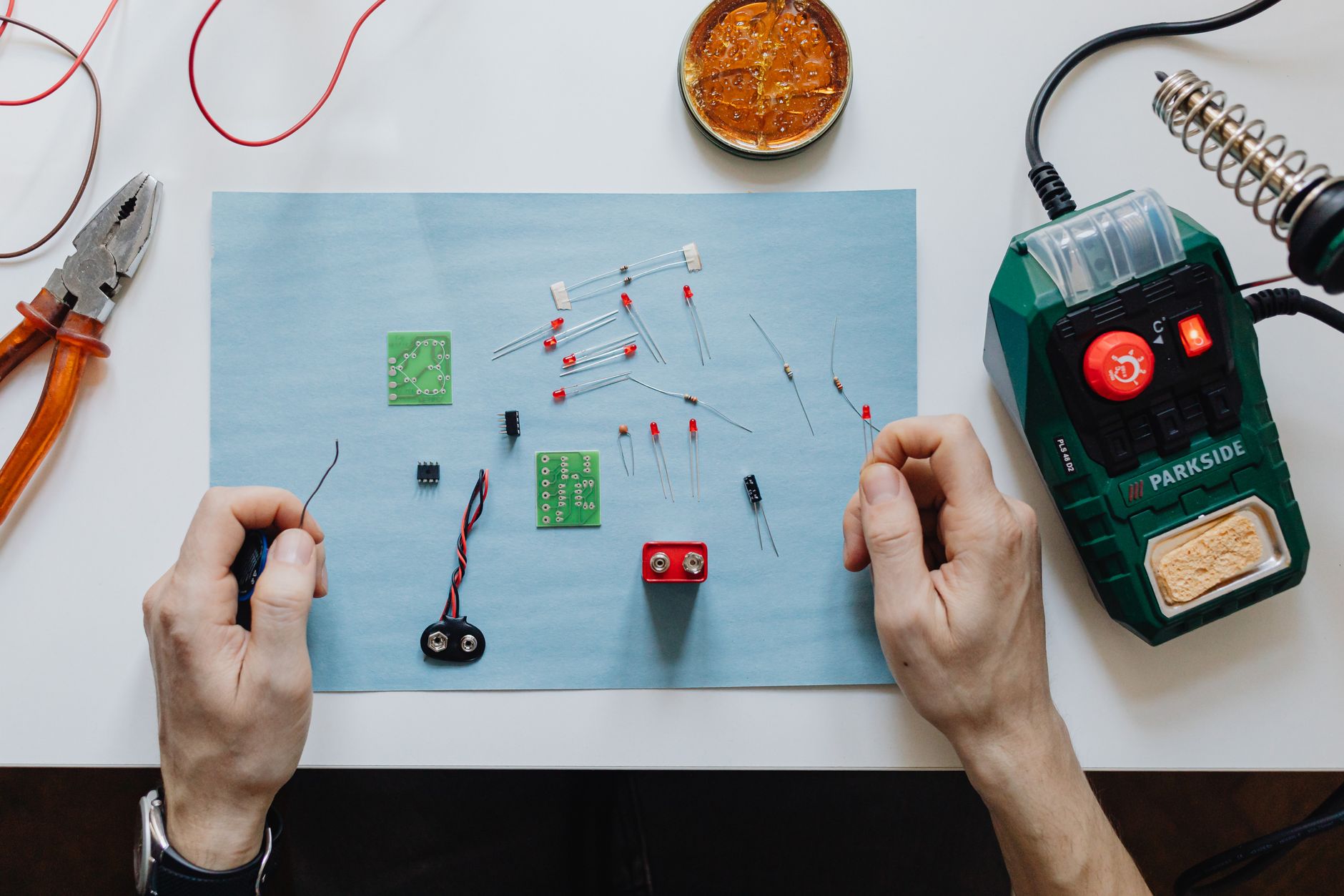 Hands-on electronics repair with tools, circuit board, and soldering station on workspace.