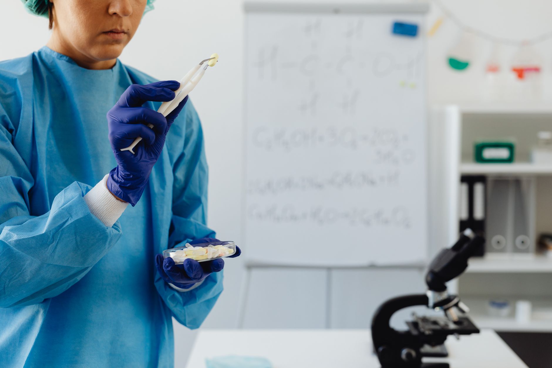 Scientist in lab coat examining samples with microscope in laboratory.