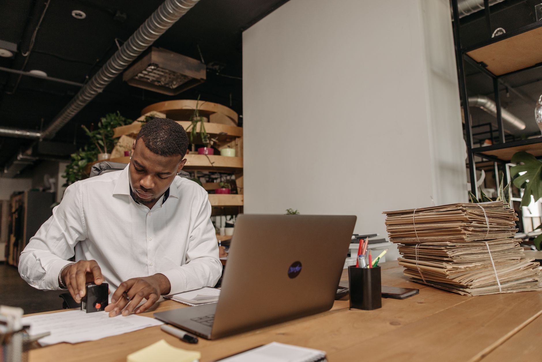 African American man focused on stamping documents at an office desk with a laptop and folders.