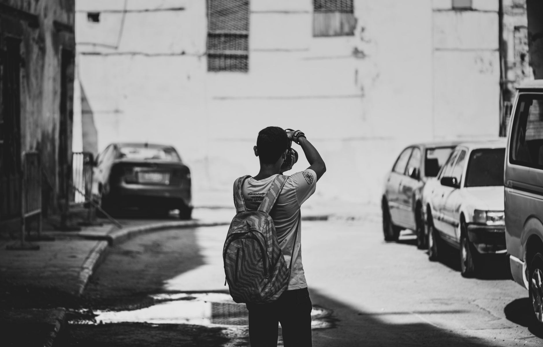 A man with a backpack photographing the city street in black and white.