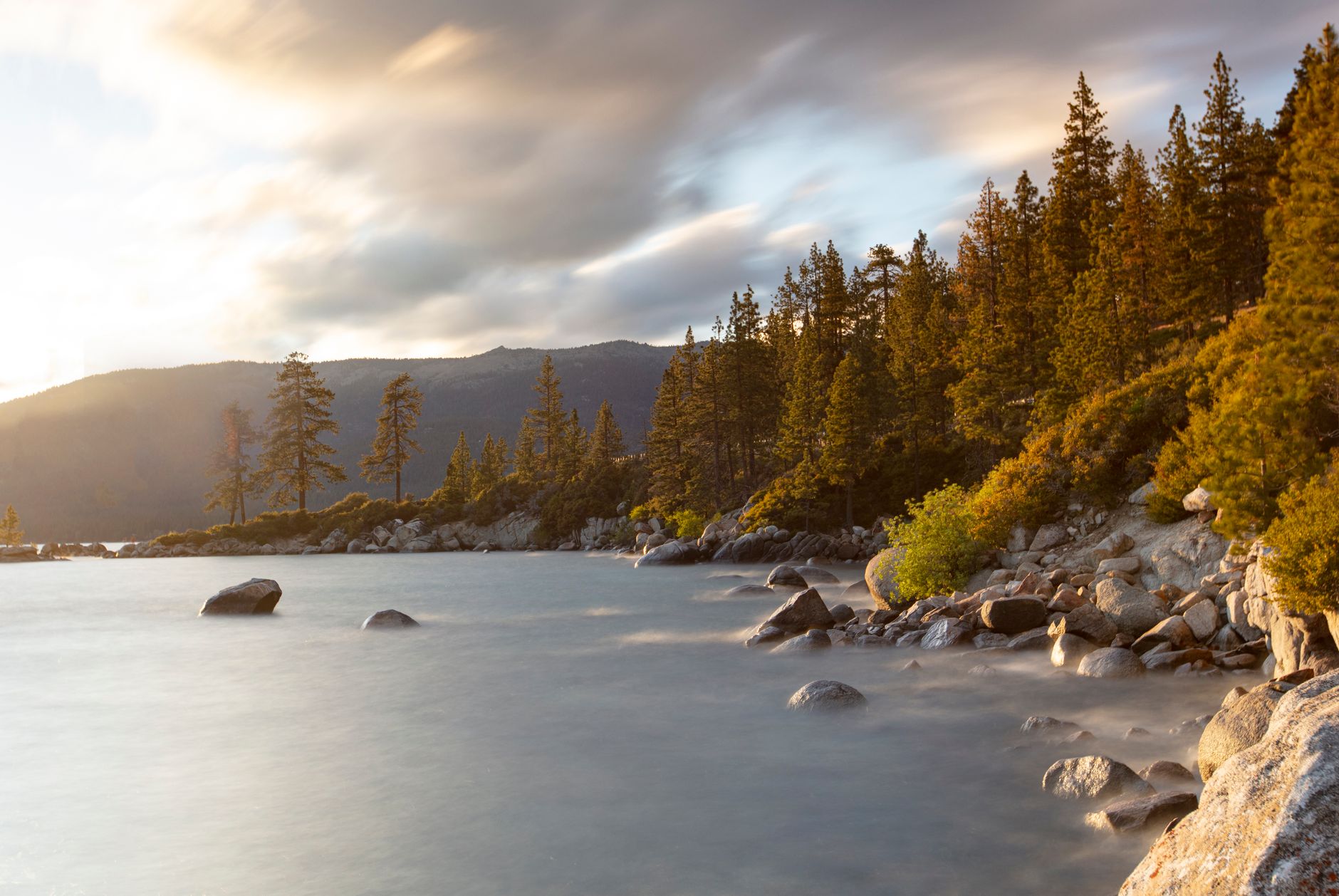 Peaceful Lake Tahoe landscape with pine trees and rocky shoreline at sunset.