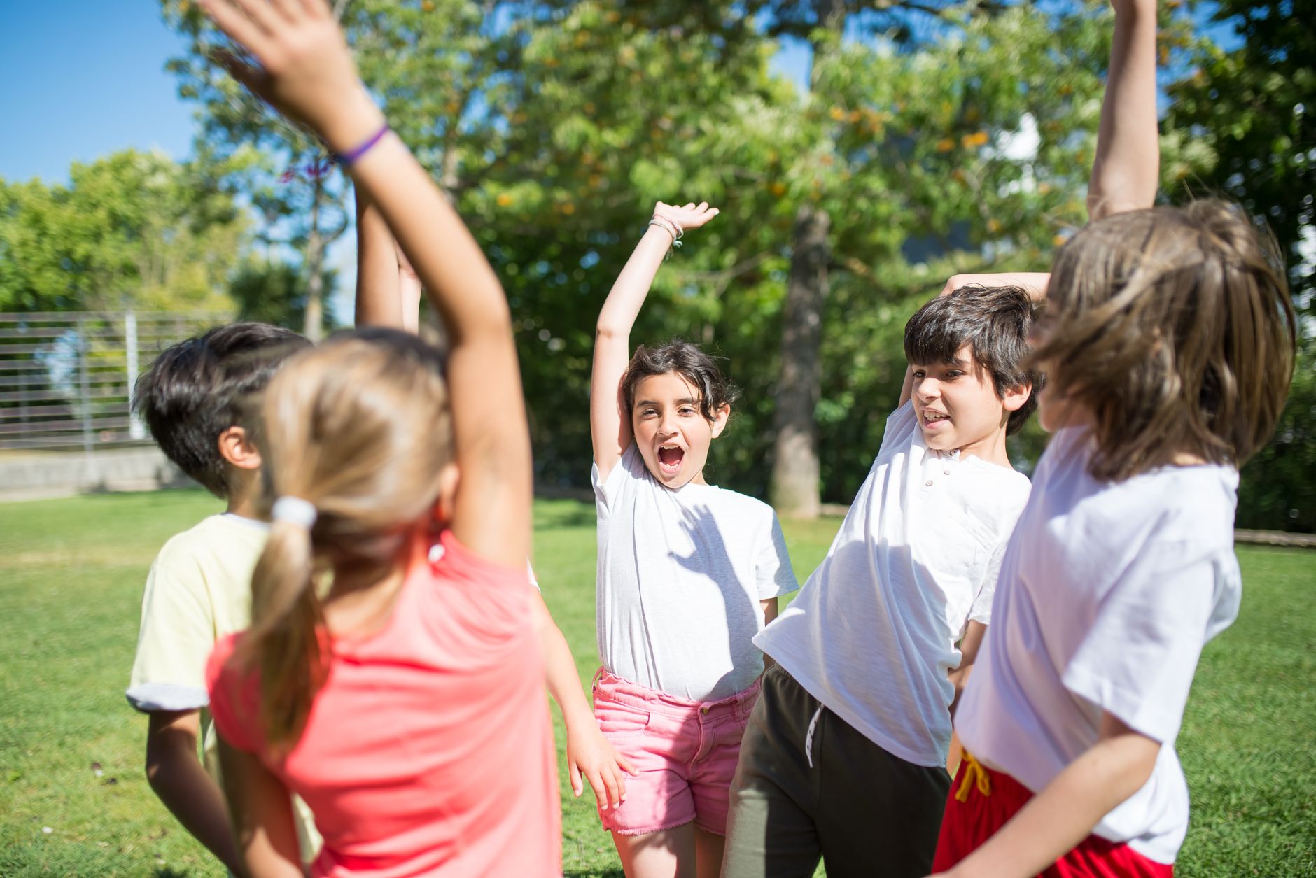 Group of children playing with raised arms in a sunny park, enjoying summer fun.