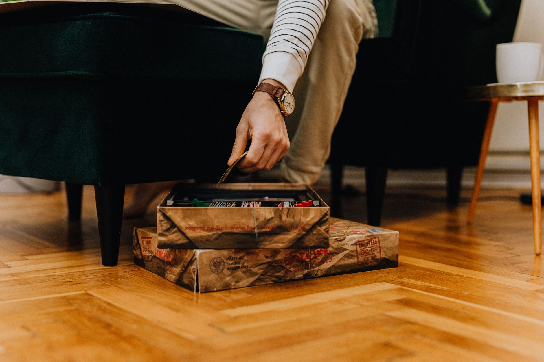 Hand reaching into an open board game box on a wooden floor in a cozy home setting.