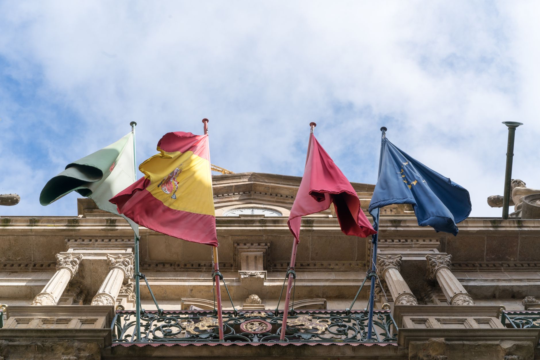 From below of Spanish flag and flags of Spanish provinces together with European Union flag waving on facade of magnificent stone building on sunny day