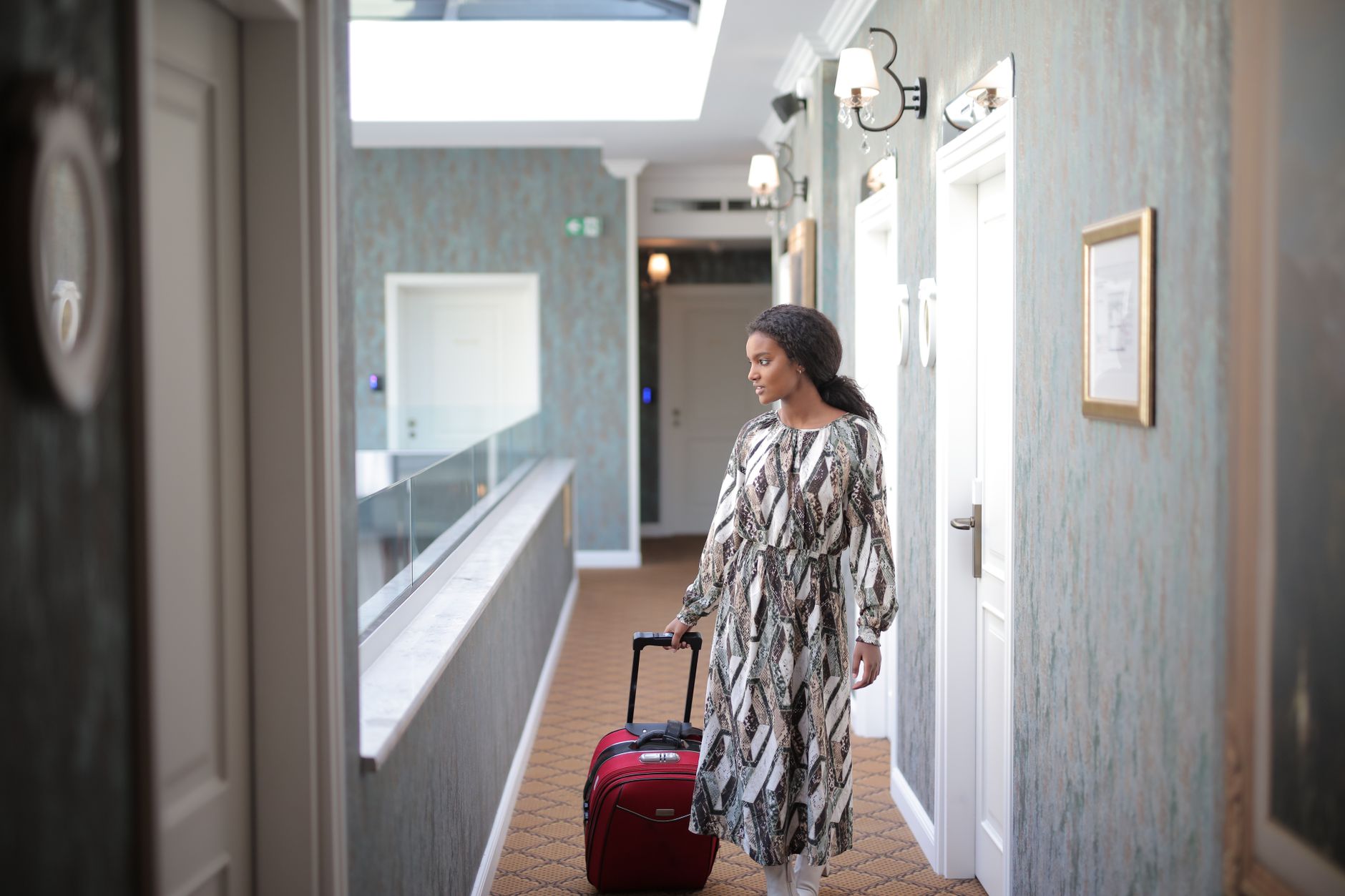 A woman walks with luggage through a stylish hotel corridor, embodying travel elegance.