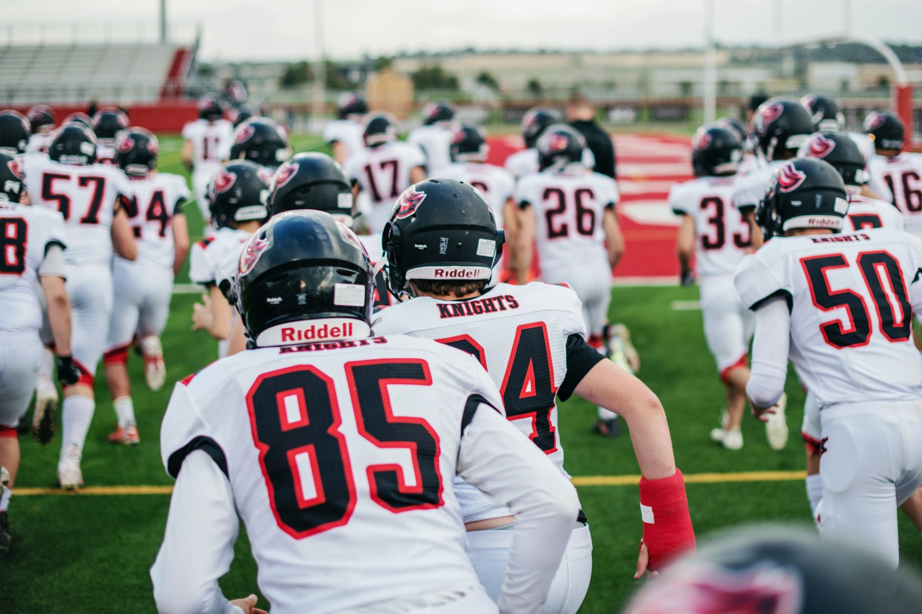 High school football team in uniforms running onto field during practice.