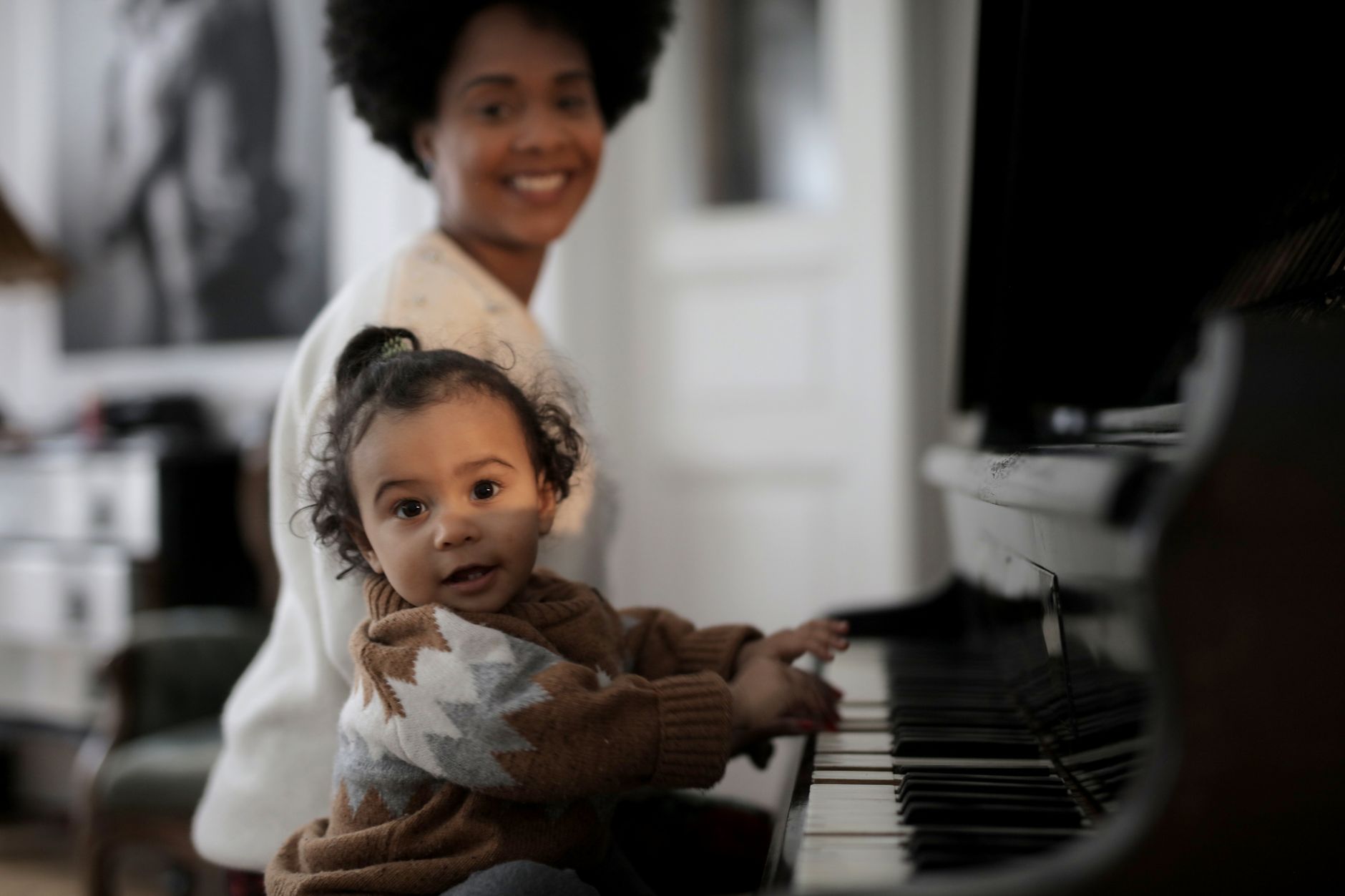Adorable toddler playing piano with a parent smiling in the background, capturing a warm family moment.