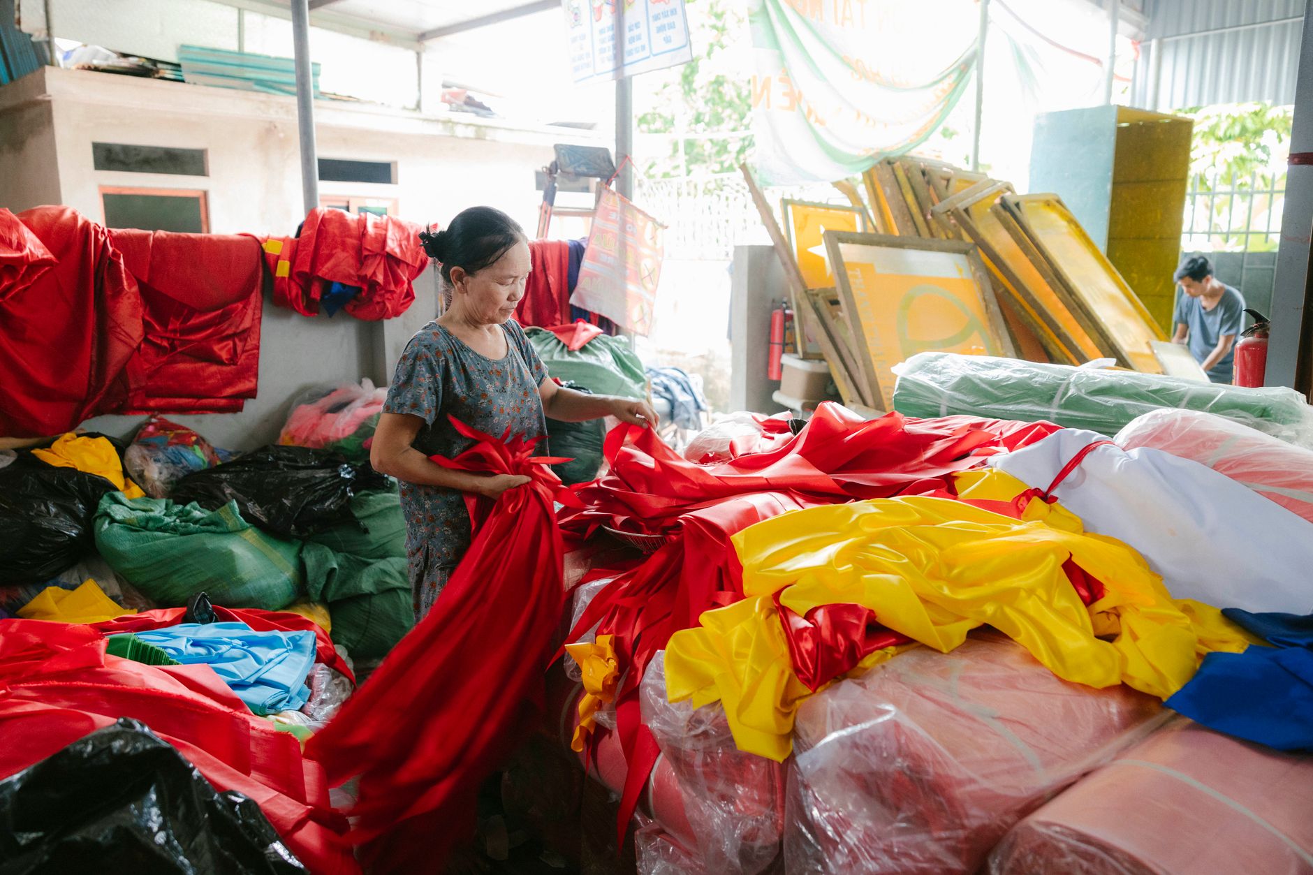 A woman meticulously sorts vibrant fabrics in a bustling textile workshop filled with colorful cloths.