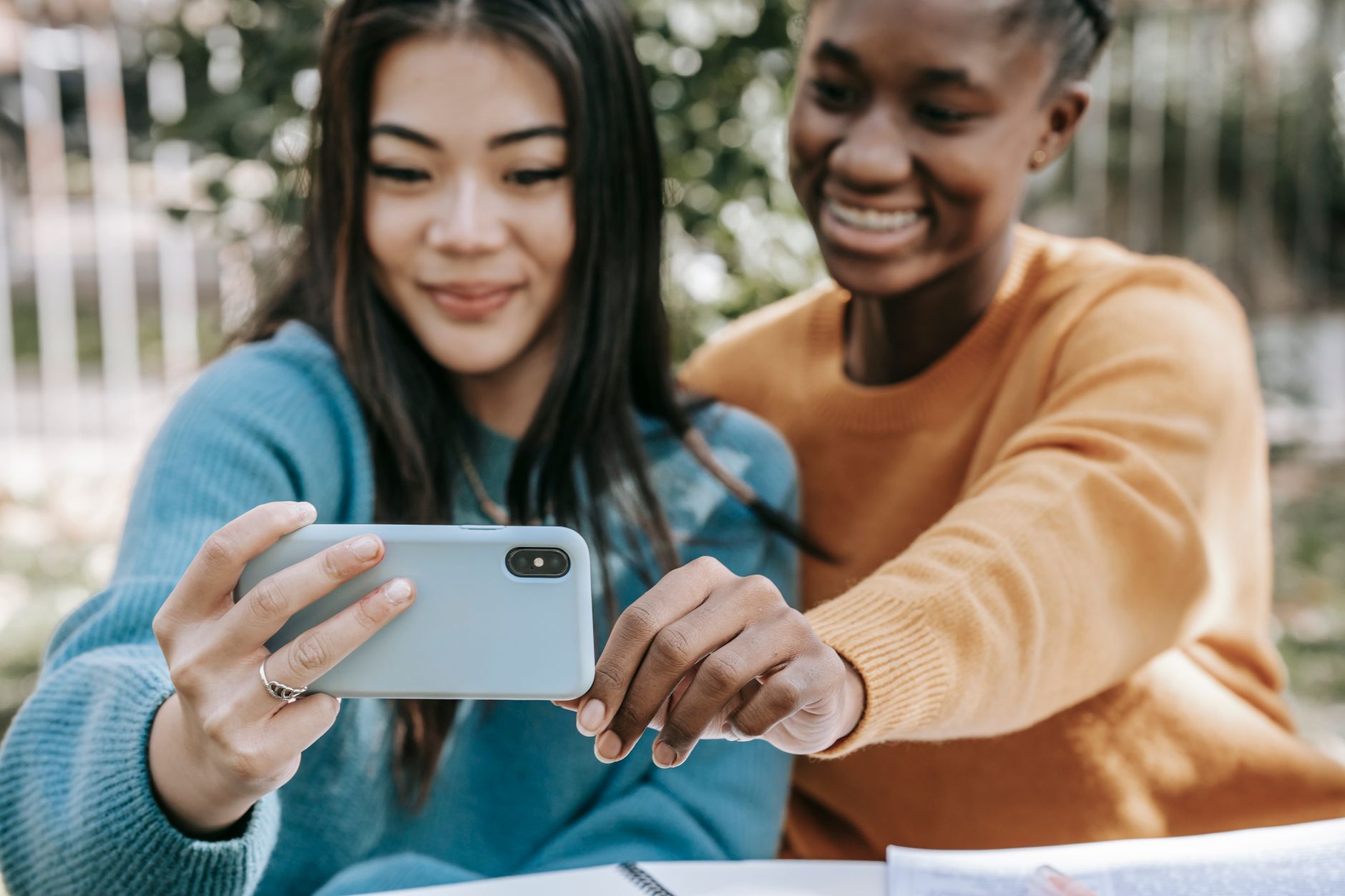 Crop happy multiracial friends taking selfie with mobile phone at table on street in daytime