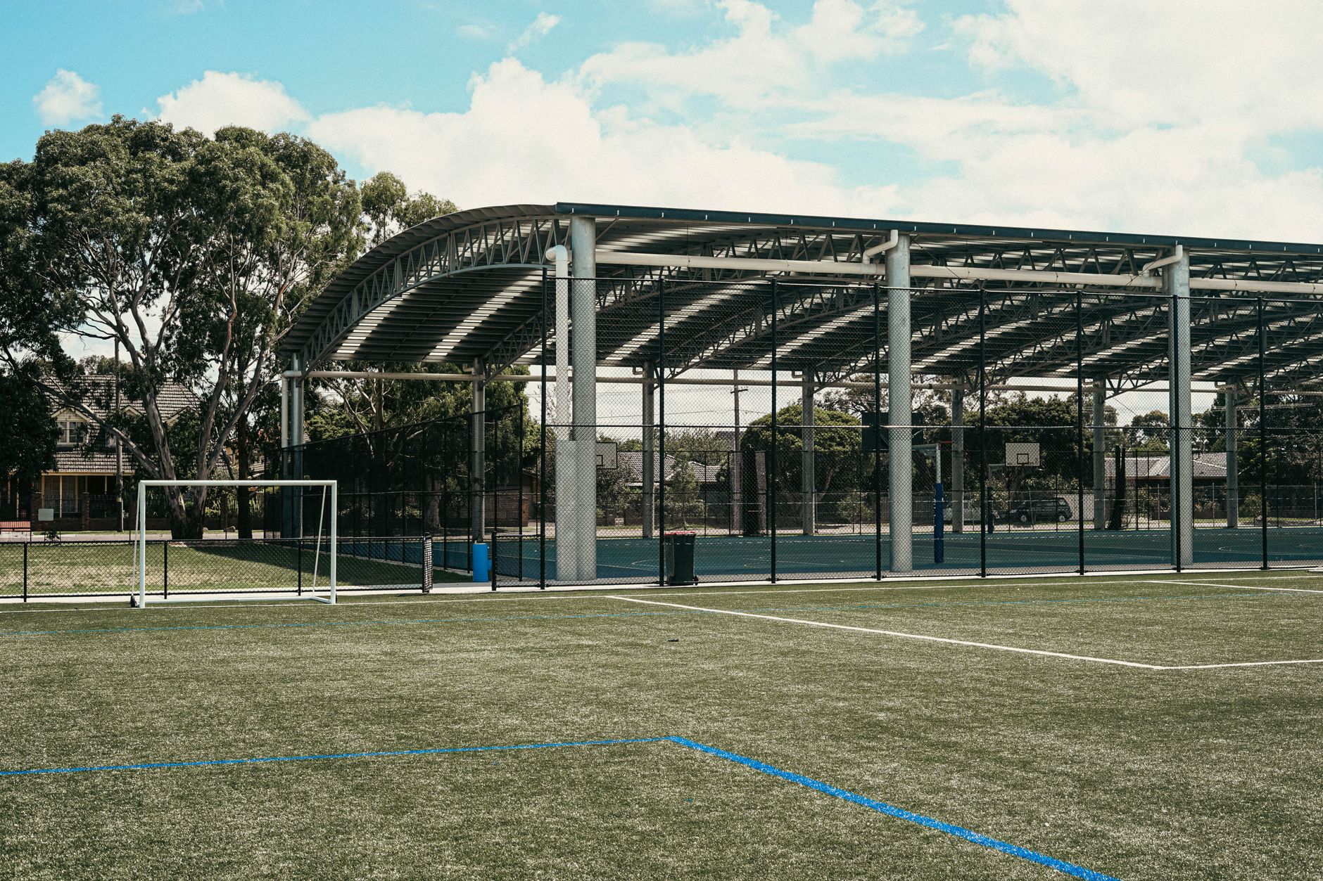 A versatile sports facility featuring a roofed court and soccer field under a bright sky.