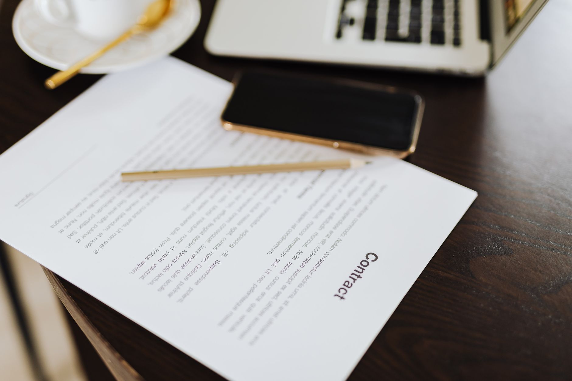 Close-up of a contract with office essentials like a laptop and coffee on a desk.