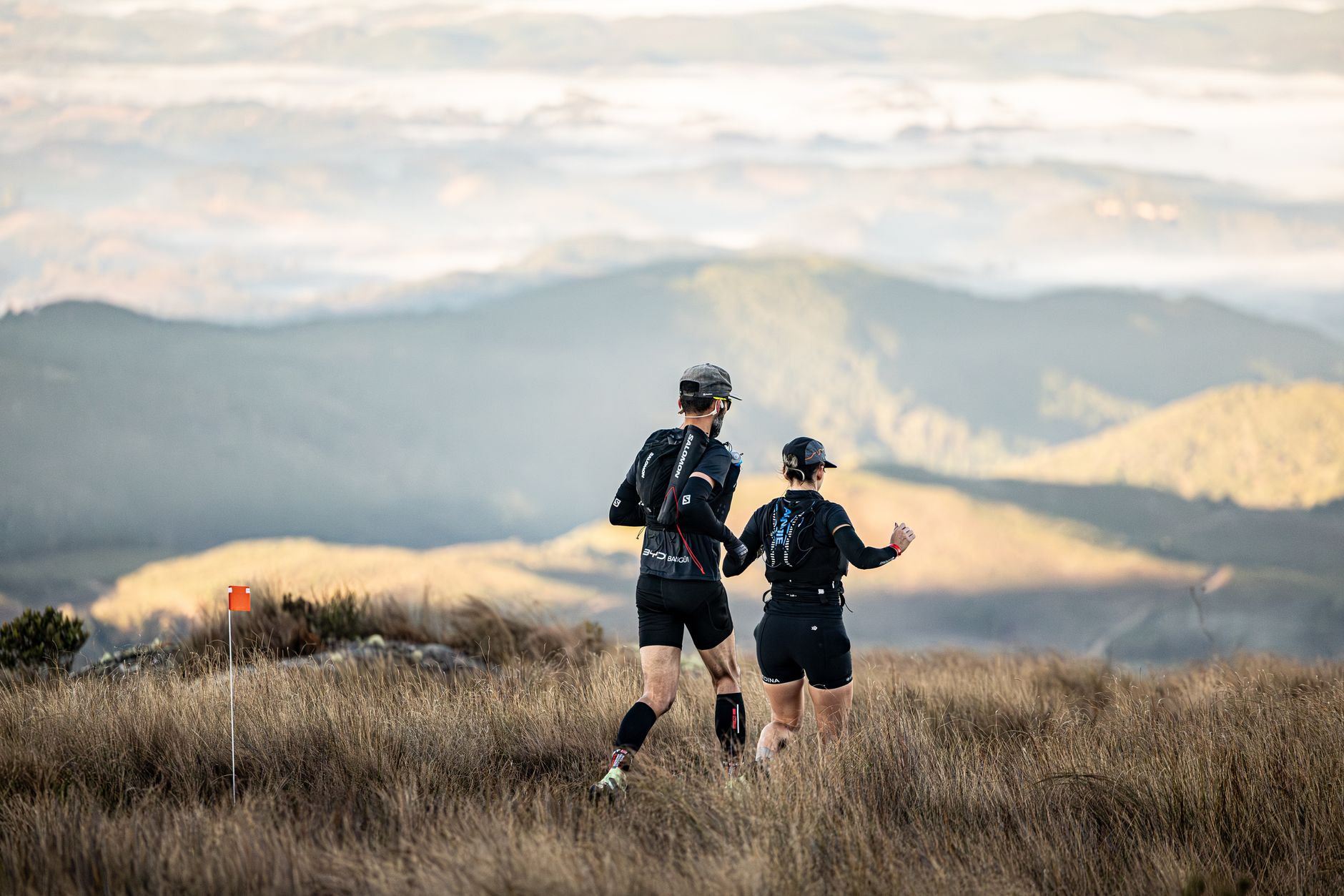 Two trail runners navigate a scenic mountain landscape during daylight hours.