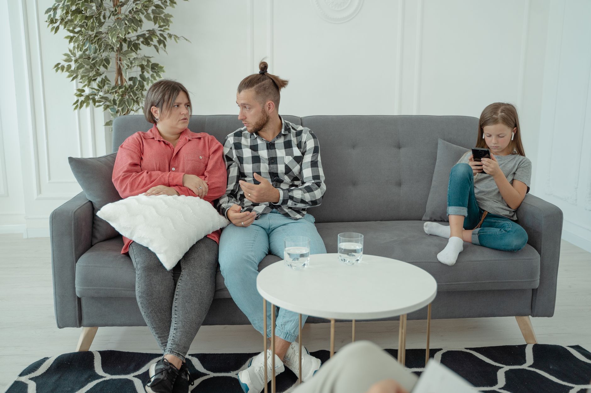 A family therapy session with parents discussing things while a child is absorbed in her smartphone.