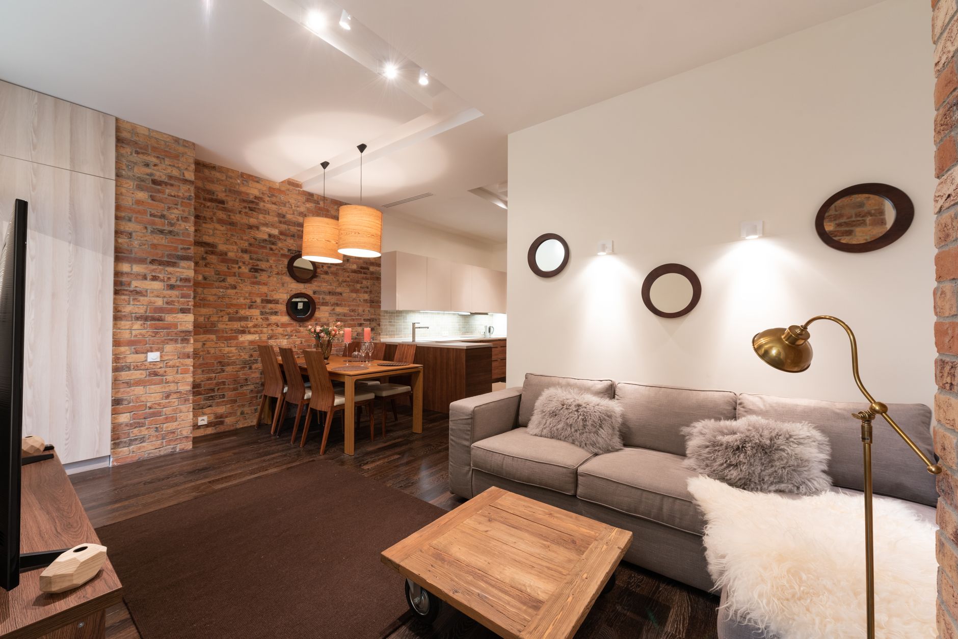 Interior of apartment with wooden table and couch with pillows near TV with cabinet and white walls near chairs and lamp
