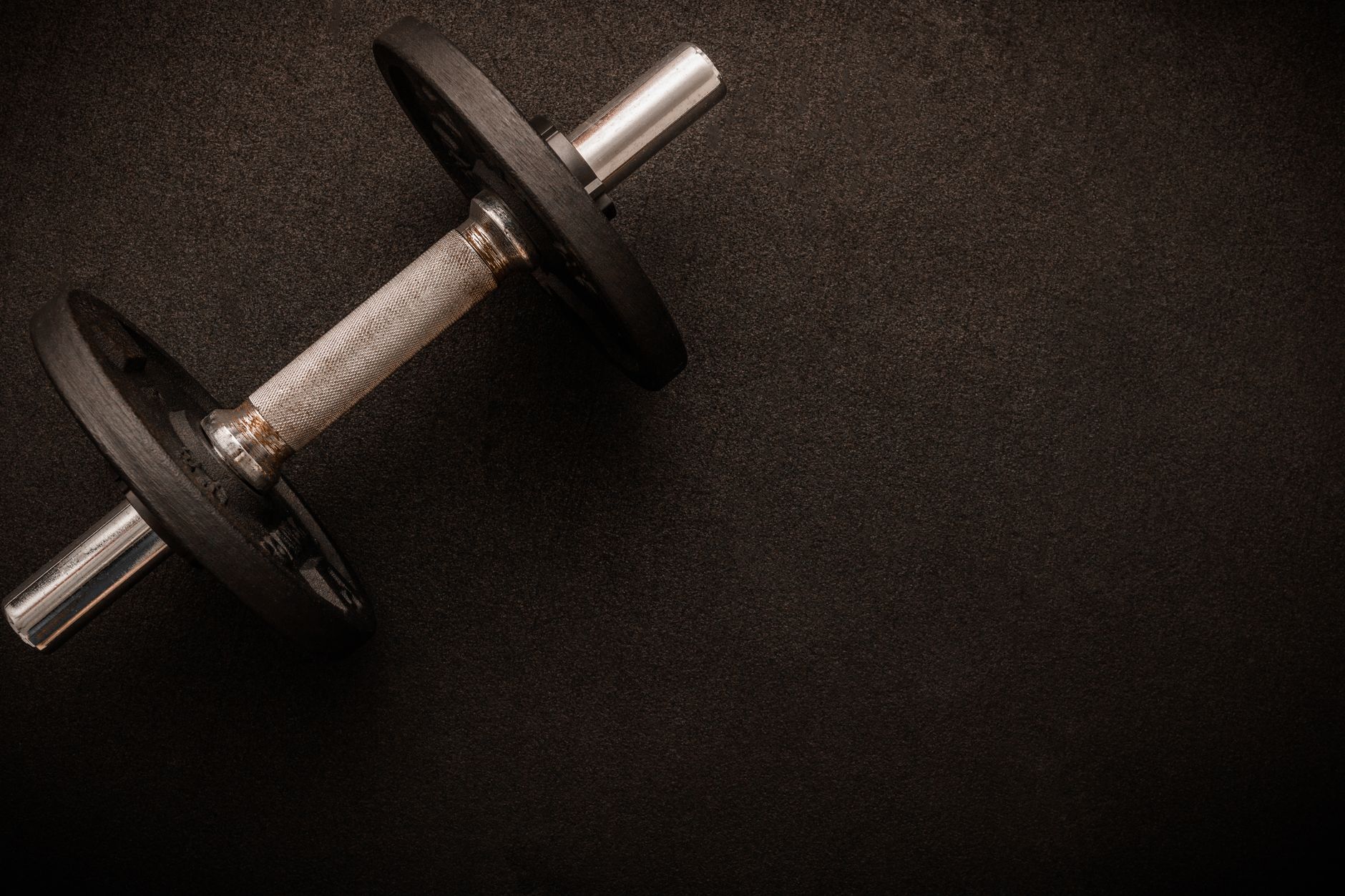 A single dumbbell placed on a dark textured surface, featuring a minimalist fitness scene.