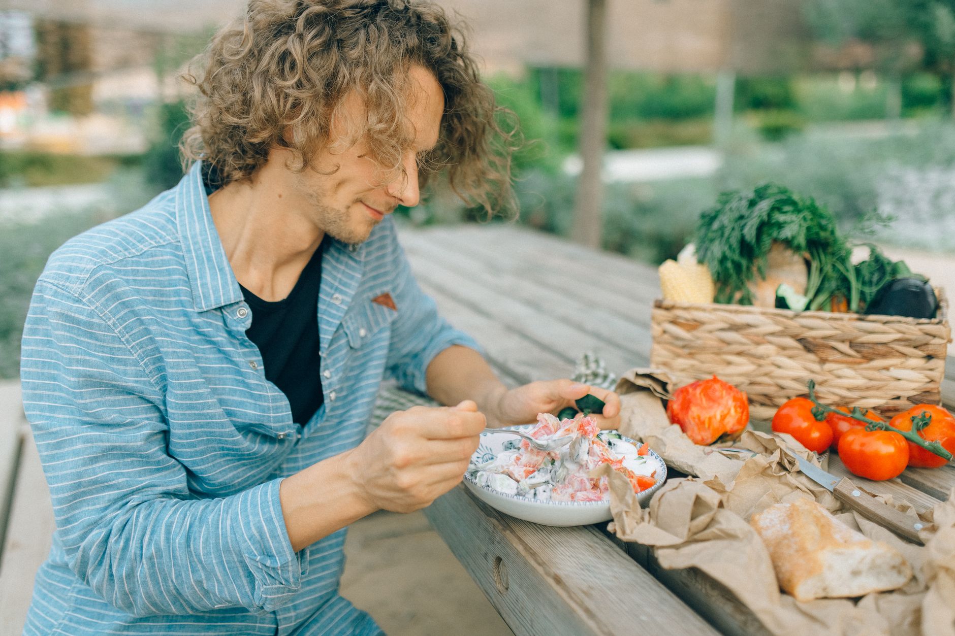 A man enjoying a healthy meal with fresh vegetables at an outdoor picnic table.