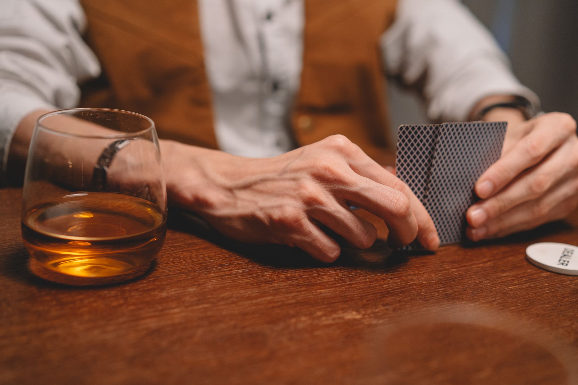 A close-up of hands holding playing cards with whiskey on the table, perfect for themes of gambling and leisure.