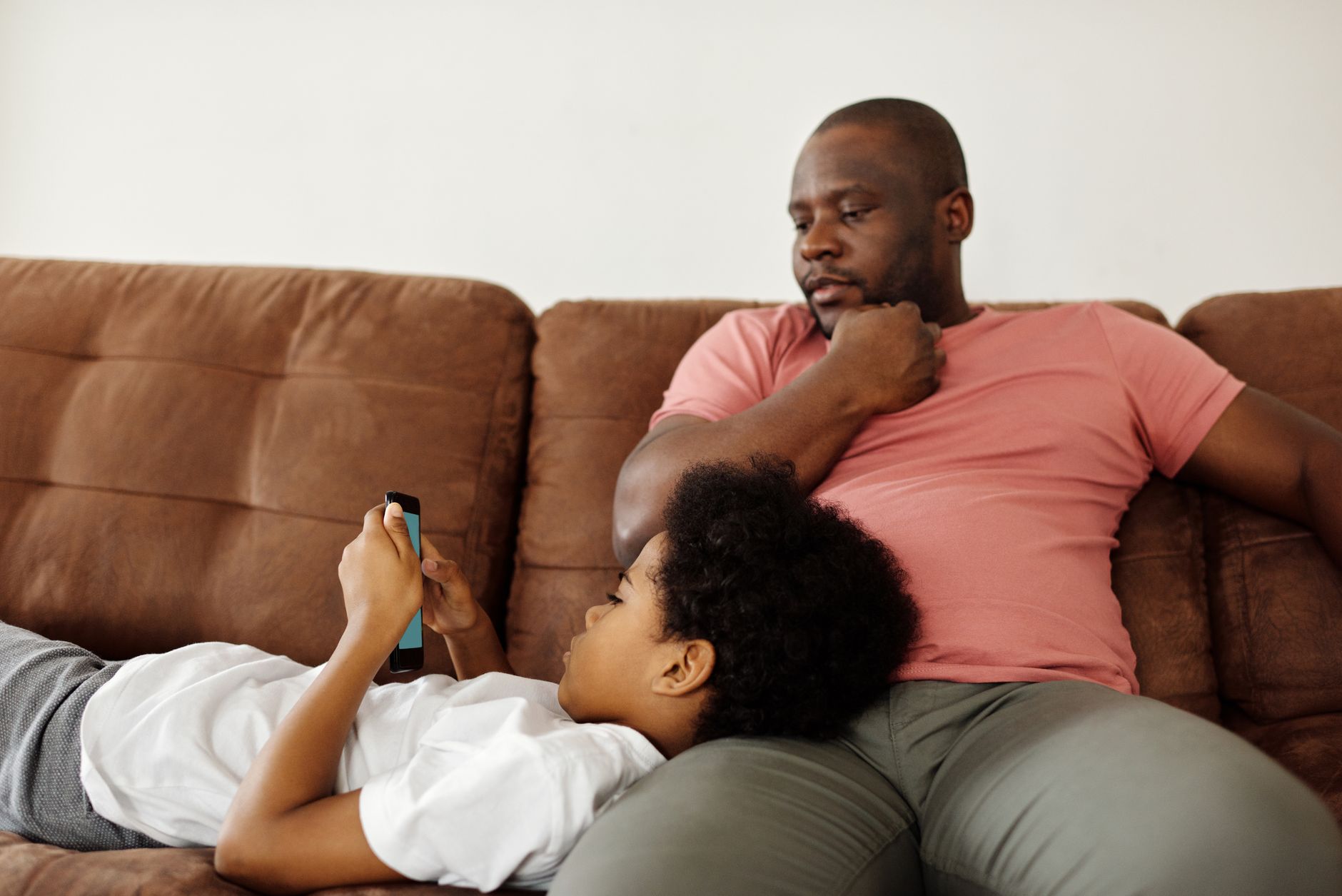 A father and child enjoying leisure time together at home on the sofa, focusing on a smartphone.