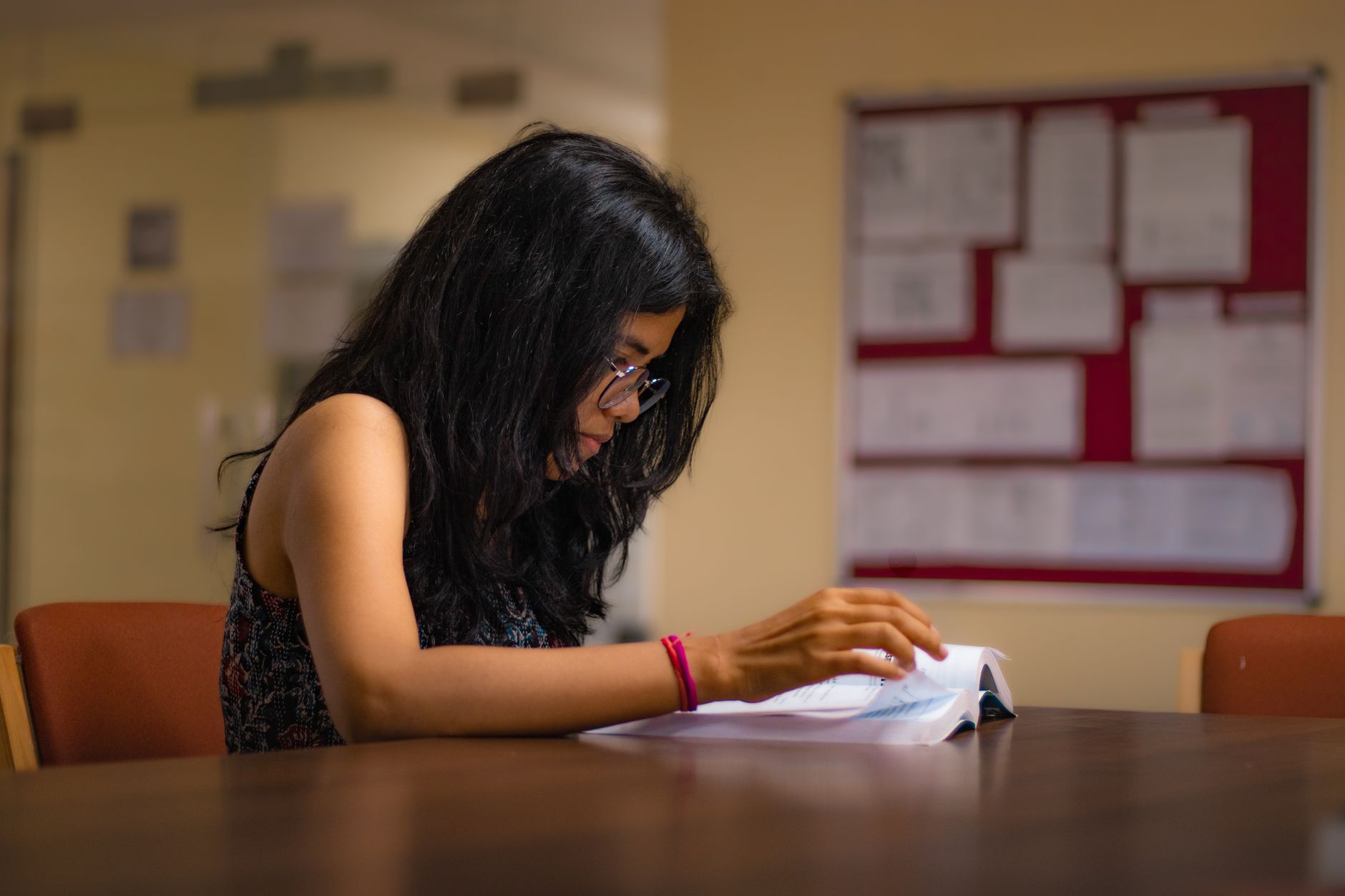 Focused young woman reading a textbook at a university library desk in New Delhi.
