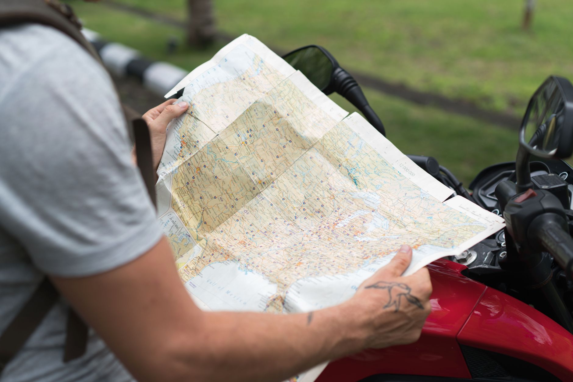 Side view of crop unrecognizable male in casual clothes with backpack sitting on motorcycle while studying city map on street