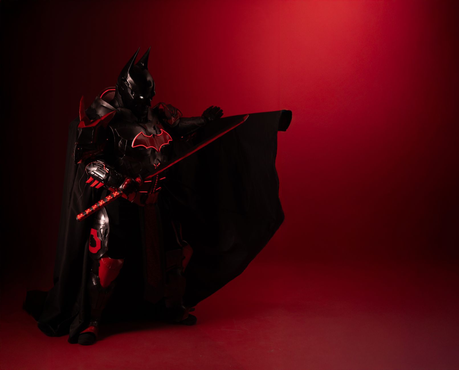 Powerful superhero cosplay in red and black armor, set against a vivid crimson backdrop.