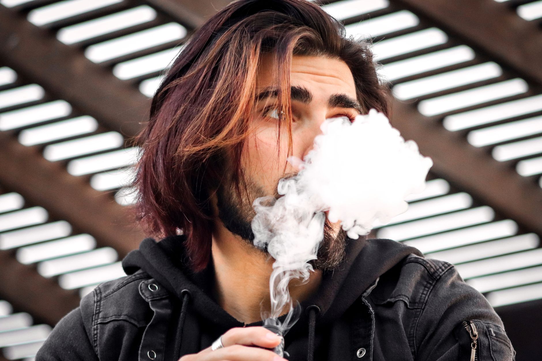 Close-up of a stylish man vaping outdoors, creating thick vapor clouds.