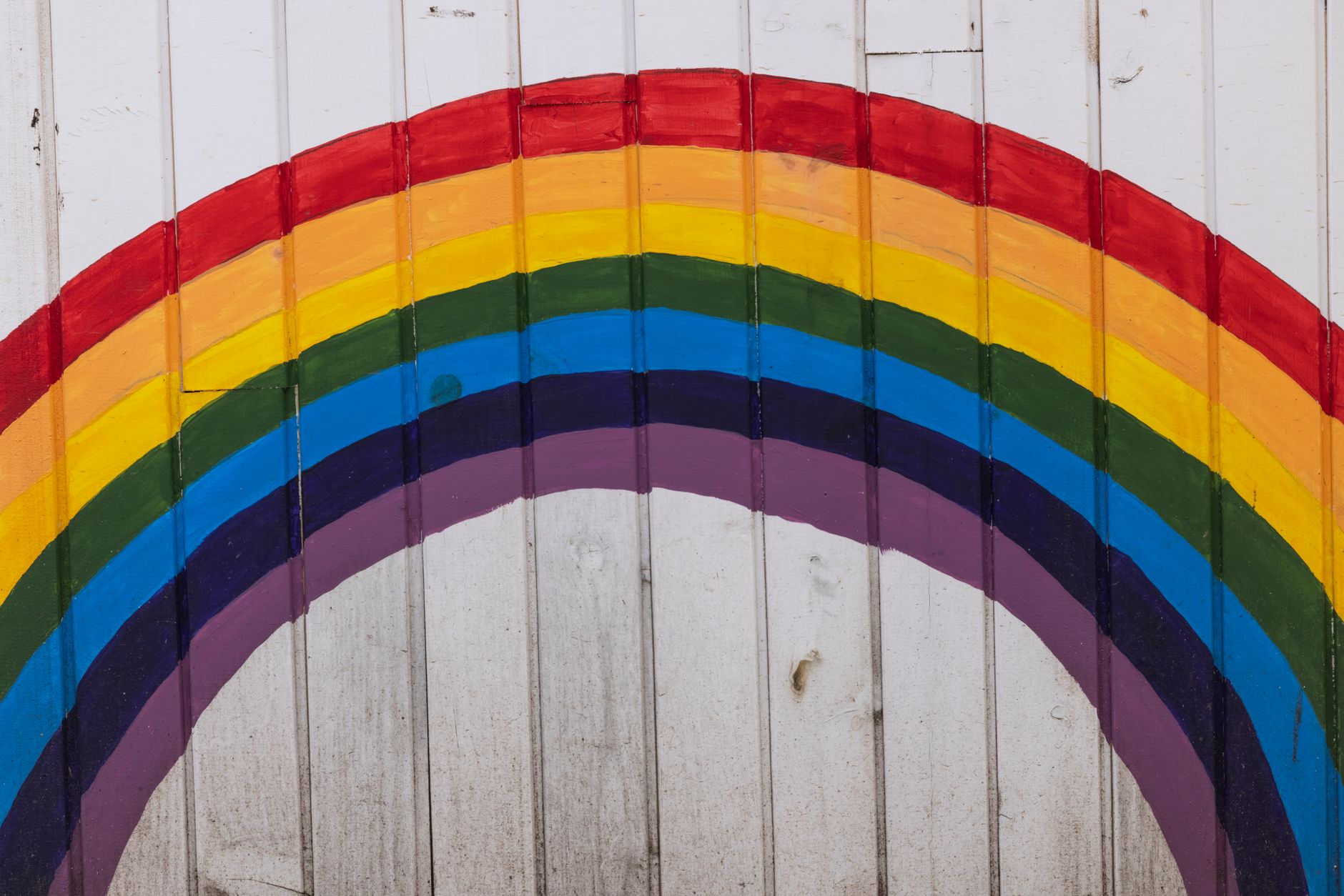 Vibrant rainbow painted on a white wooden wall, symbolizing hope and diversity.