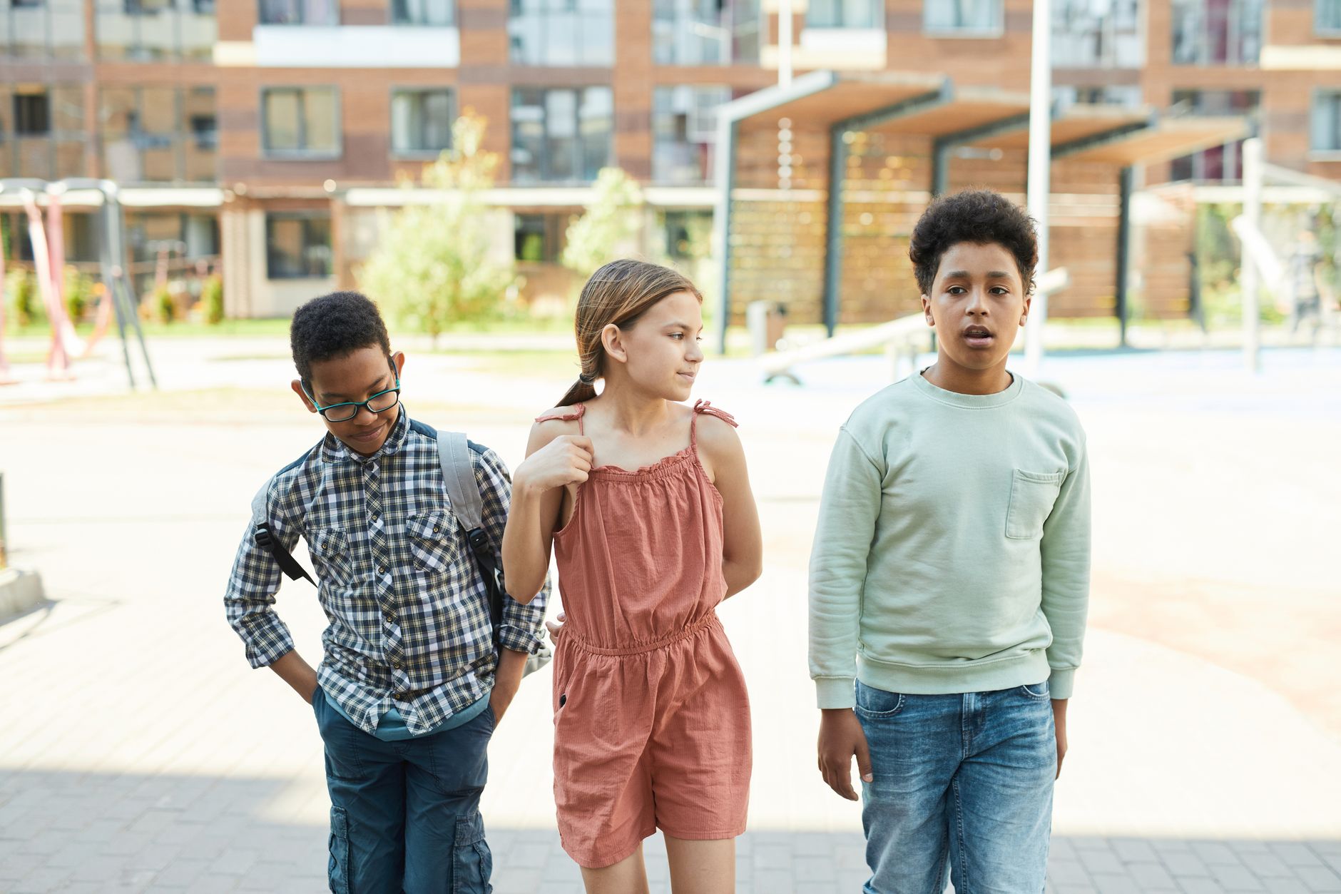 Three children walking outdoors near a city school, showcasing diversity and togetherness.