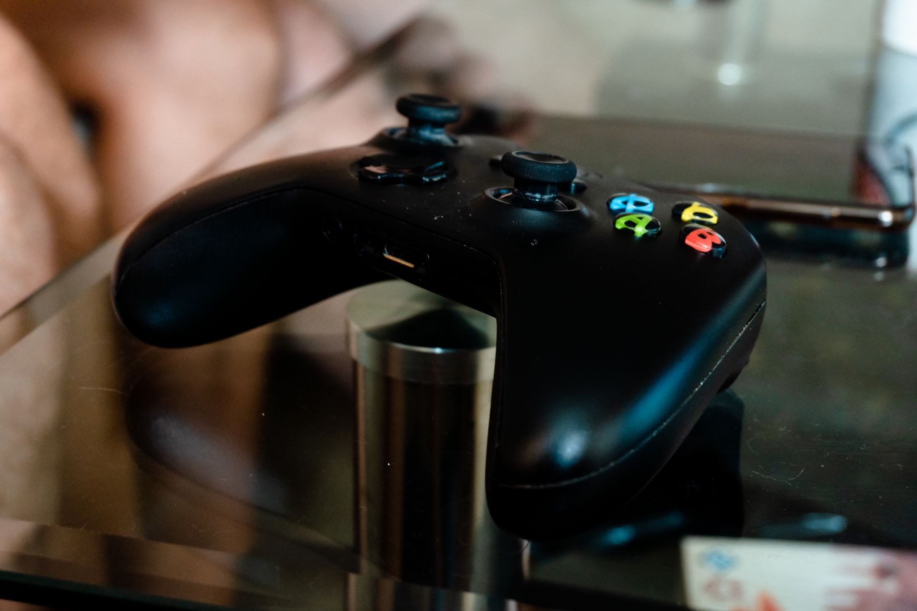 Close-up of a modern black video game controller resting on a glass table indoors.