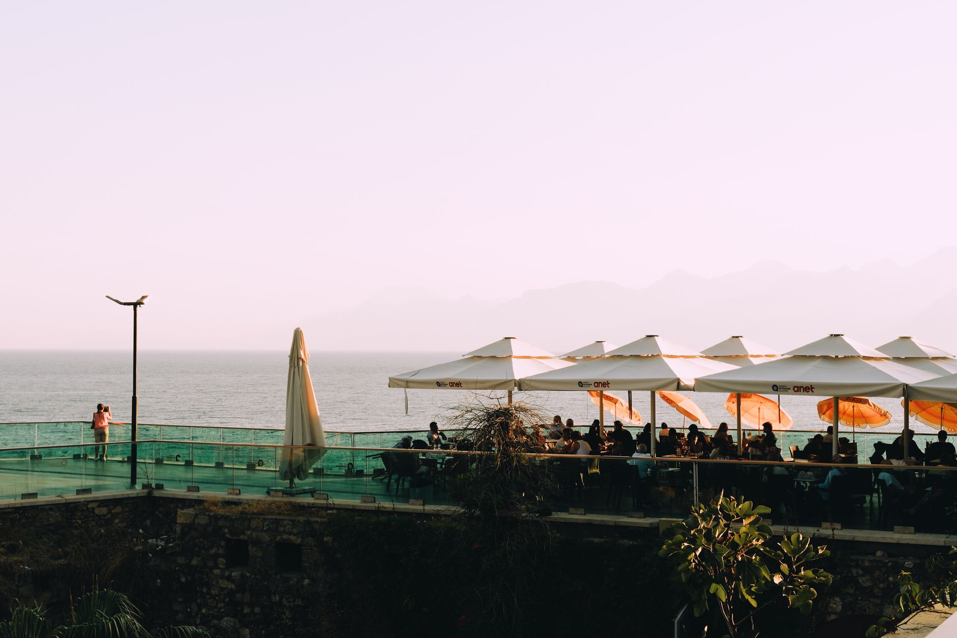 Outdoor restaurant terrace with ocean view, parasols, and people dining at sunset.