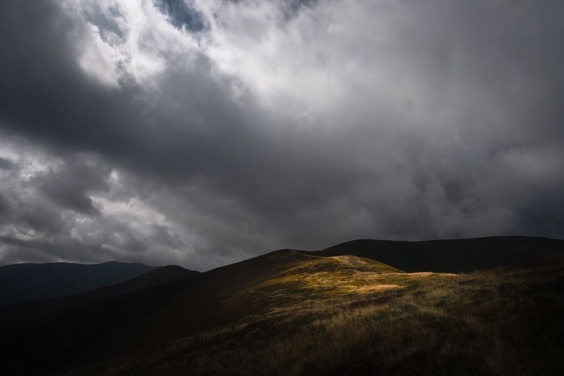 A dramatic mountain landscape with clouds and sunlit hills under stormy skies. Perfect for weather-related themes.