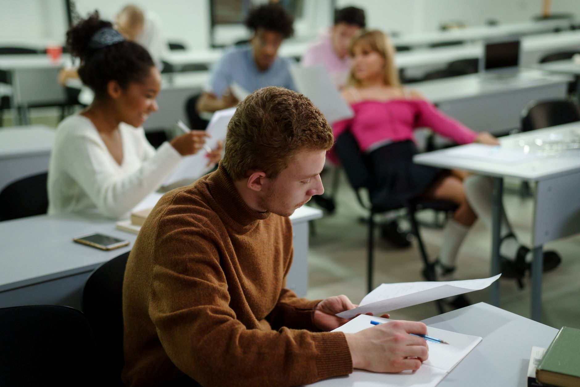 A group of diverse university students focusing on assignments during a classroom lecture.